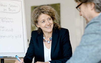 Frau mit schulterlangen lockigen Haaren unterhält sich mit einem Mann mit Brille